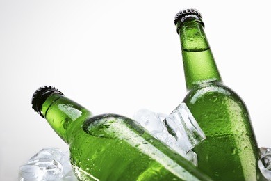green beer bottles on ice over white background