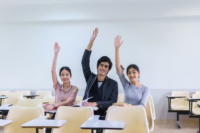 three people young asian man and woman student raising hands in a classroom showing ready answer. concept of education, vote, presentation, meeting and seminar.