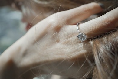 close up of an elegant engagement diamond ring on woman finger while touching her hair under sunlight. split tone instragram like process. love and wedding concept.