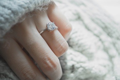 close up of an elegant engagement diamond ring on woman finger with dark gray sweater winter clothe background. love and wedding concept. soft and selective focus.