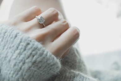 close up of an elegant engagement diamond ring on woman finger with dark gray sweater winter clothe. love and wedding concept.