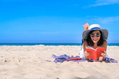 woman happy smiling and read books on the beach on a beautiful . pretty girl asian in casual looking away and smile , laughing. the beach beautiful at bright sky
