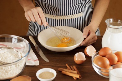 woman mixing eggs in ceramic bowl for dough on wooden table. cooking process for step by step recipe.