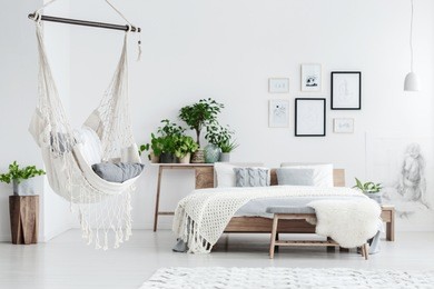hammock hanging in bright bedroom with potted plants, woolen coverlet on the bed and posters on white wall