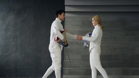 two fencers man and woman shake hands each other at the end of fencing competition indoors