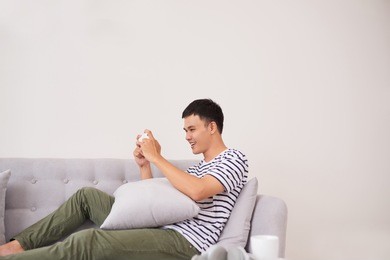 young asian man sitting on sofa and playing games on phone at home