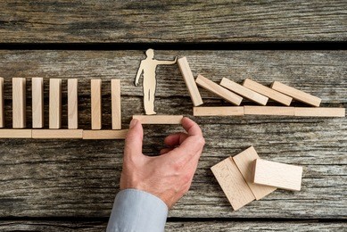 conceptual of life insurance with the hand of a man offering support through a stable platform to a paper man stopping the collapse caused by wooden bricks.