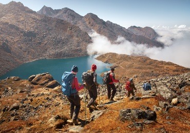 group of tourists with backpacks descends down mountain trail to lake during a hike in the national park lantang, nepal.
beautiful inspirational landscape, trekking and activity.