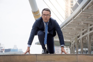 asian businessman in suit preparing to run,getting ready to run the race with modern building on the background