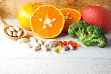 multivitamins and supplements in wooden spoon with fresh fruits on white wooden background.