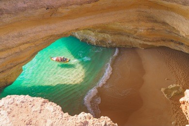 a boat with tourists leaves a cave at the algarve coast in portugal. view through a hole in the ceiling from above.