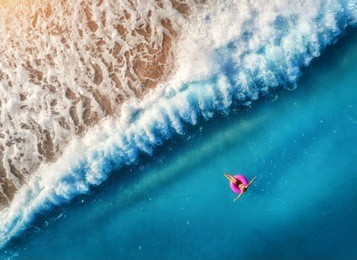 aerial view of young woman swimming on the pink swim ring in the transparent blue sea in oludeniz,turkey. summer seascape with girl, beautiful waves, azure water at sunset. top view from drone. travel