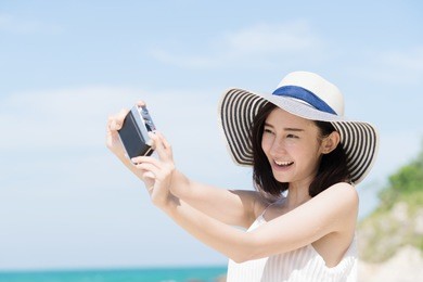 young asian woman selfie by camera on the beach with sunny day. happy girl selfie and smile with blue sky. travel and lifestyle summer concept.