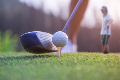 wood driver in proper address of the woman golf player on tee off at golf club, ready to hit and impact away to the fairway ahead, with playermate waiting in background
