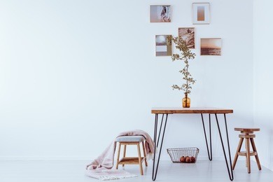 orange vase with branch on table in simple dining room with stools and pictures on a wall with copy space