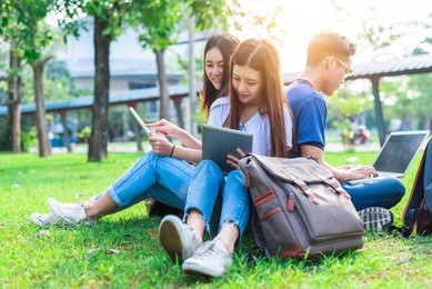 group of asian college student using tablet and laptop on grass field at outdoors. technology and education learning concept. future technology and modern entertainment concept. edutainment theme.