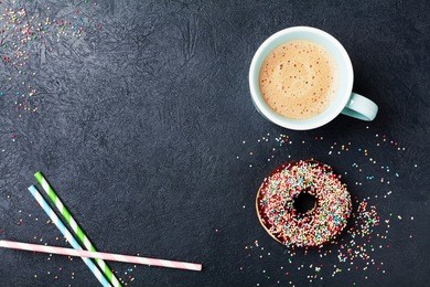 cozy breakfast with colorful donut and fresh coffee on black table top view. flat lay. copy space