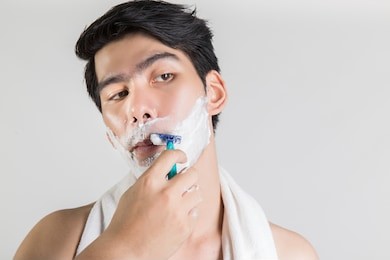 asian handsome man is shaving looking away, white isolated