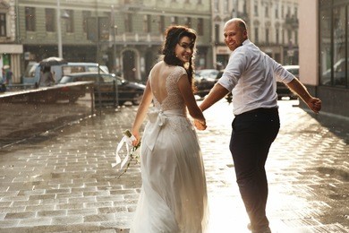 beautiful wedding couple looks happy walking around the city in the rain