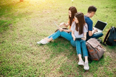 a group of young or teen asian student in university smiling and reading the book and look at the tablet or laptop computer in summer holiday.