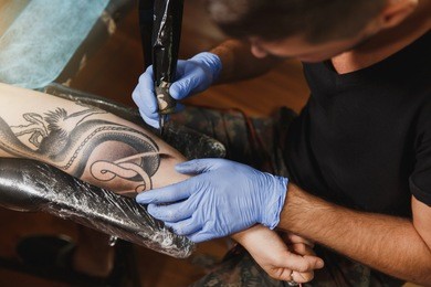 close up of professional tattooer artist doing picture on hand of man by machine black ink from a jar. tattoo art on body. equipment for making tattoo art. master makes tattooed in light studio