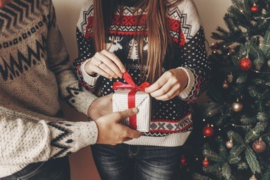 happy couple in stylish sweaters holding gift with bow in festive room at christmas tree. atmospheric festive moments. merry christmas and happy new year concept. space for text