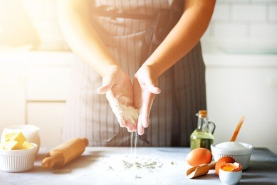 female hands kneading dough, baking background. cooking ingredients - eggs, flour, sugar, butter, milk, rolling pin on white style kitchen. copy space