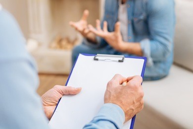 useful notes . selective focus of how skillful male psychologist putting diagnosis on the paper while holding folder and pencil and patient sitting in front of him