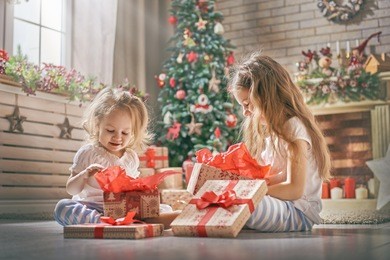 merry christmas and happy holidays! cheerful cute childrens girls opening gifts. kids wearing pajamas having fun near tree in the morning. loving family with presents in room.