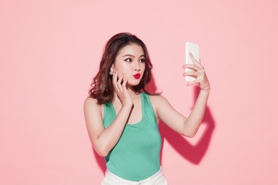 asian young woman taking selfie photo on pink background.