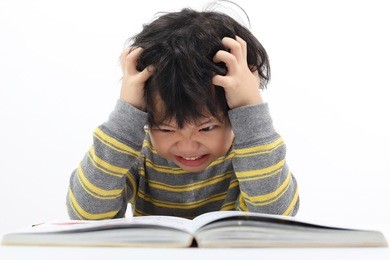 little asian boy frustrated over homework with his both hand on head.. boy studying at table isolated on white background.