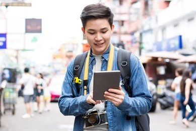 asian photographer tourist backpacker using tablet to find location while traveling on holiday in khao san road thailand