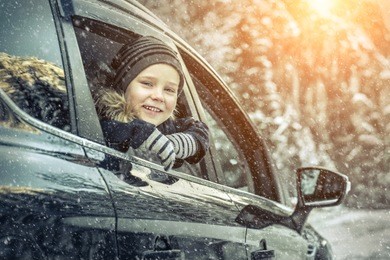 happiness caucasian smilling boy looking out of black car window in sunny day at winter time near the forest.