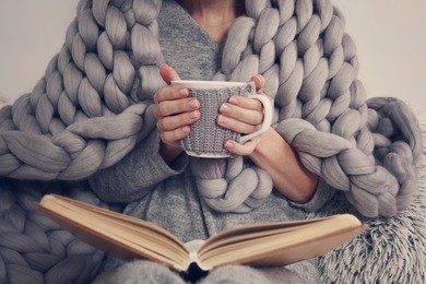 cozy woman covered with warm soft merino wool blanket reading a book. relax, comfort lifestyle.