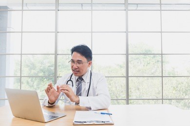 senior asian doctor or teacher or expert making video call or live video on social network with patient or student while sitting on modern office or hospital. concept of education or technology,health
