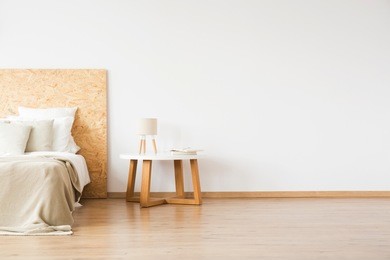 small table with a lamp and books standing by the bed in white bedroom interior