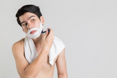 asian man is shaving looking away, white isolated