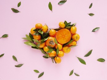 heart made from fruits. composition of small tangerines with leaves and persimmons on a pink background. pattern of fruits, top view, flat lay.