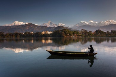 beautiful landscape with phewa lake and boat on lake, mountains in background also as reflectaion on lake.  machapuchare-fishtail, annapurna and many others. pokhara, nepal