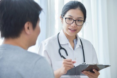 asian female doctor examining and taking note on checklist paper with male patients in medical room.
