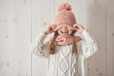 winter portrait of happy little girl wearing knitted hat, scarf and sweater. child on white wooden background. fashion concept.