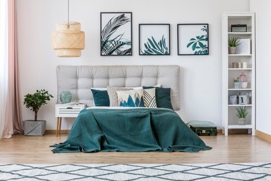 plant, white cupboard and rattan lamp in green bedroom interior with bed with beige bedhead and leaves posters on the wall
