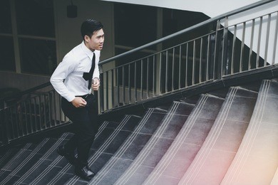 young asian businessman holding brown leather bag working on staircase go office hurry work time with sunset top view and vintage tone