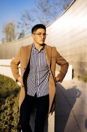 confident successful man in glasses and a fashionable beige coat posing in the sun in the park
