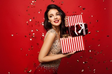 beautiful girl standing on a red background with a gift in the hands smiles a lovely smile. celebration of christmas in the office,or new year