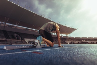 rear view of an athlete on his mark ready to sprint on running track. runner using a starting block to start his run on race track in a stadium.