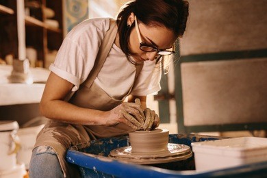 woman moulding clay on pottery wheel. craftswoman making pot in workshop.