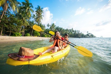 asian boy and girl play kayak boat on the beach in troppical resort in koh kood island, thailand