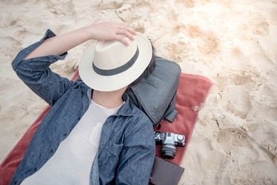 young asian man lying on the beach and close his face by hat, vacation time and summer holiday concepts