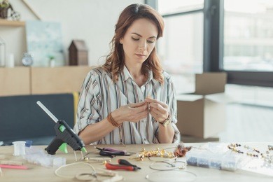concentrated young woman making accessories of beads in workshop